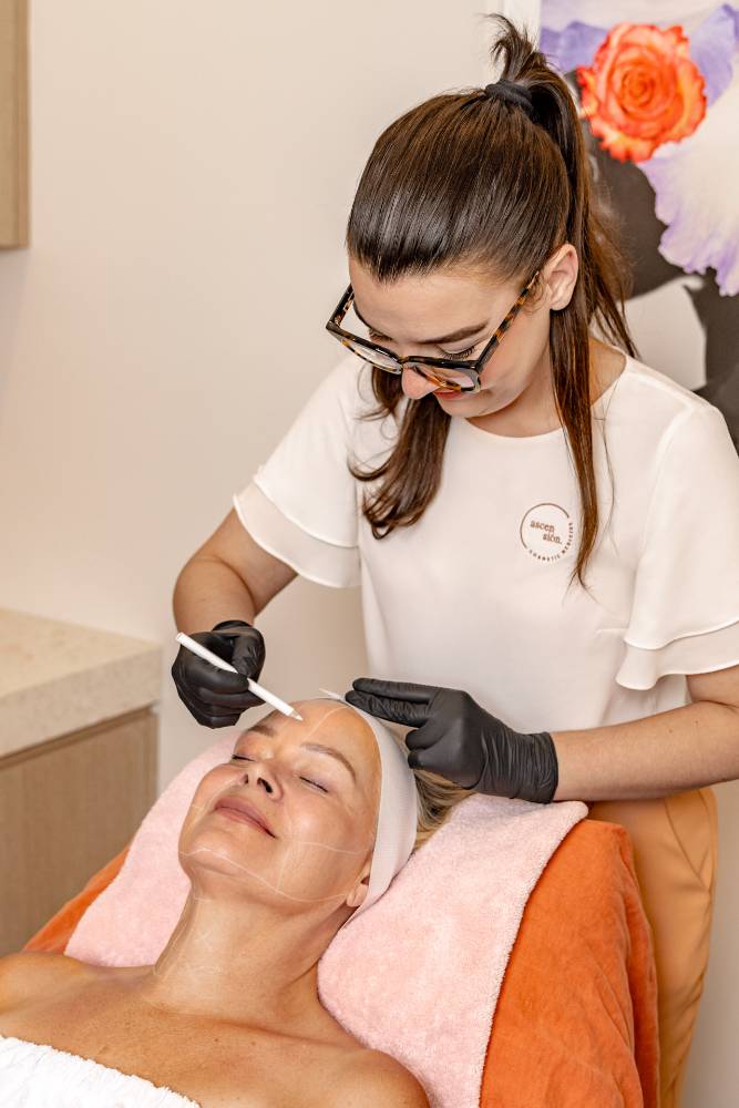 A skincare specialist in white attire performs an Ultraformer MPT facial treatment on a content client, using a pen-like device for skin rejuvenation and tightening
